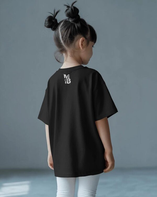 Child wearing an oversized black MIB T‑shirt and white leggings, standing with their back to the camera against a minimalist blue‑grey background.