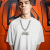 Person wearing an oversized white T‑shirt and a silver motorcycle pendant necklace standing in front of a bold orange wall with black graphic lettering, creating an urban streetwear aesthetic.