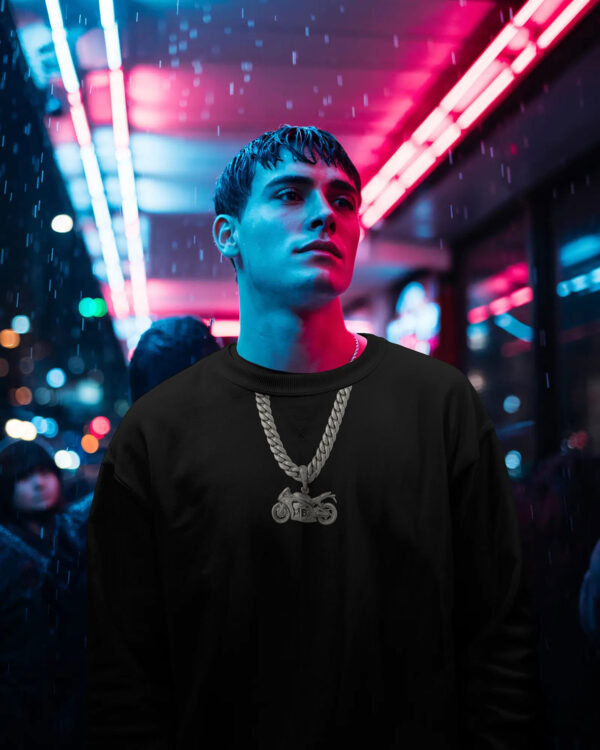 Person wearing a black sweatshirt and motorcycle chain pendant standing under neon lights in a rainy night time city scene