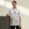 Person wearing a white T‑shirt with a bold printed chain-and-motorcycle pendant graphic, leaning against a block in a minimal studio setting for a clean urban streetwear look.