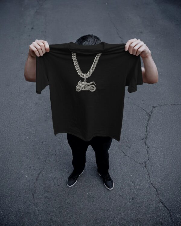 a man holding up a black t-shirt in the air covering his face, with a platinum chain with a motorbike pendant design on the front.