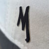 close up of an black MIB logo M on the side of a cream cap.