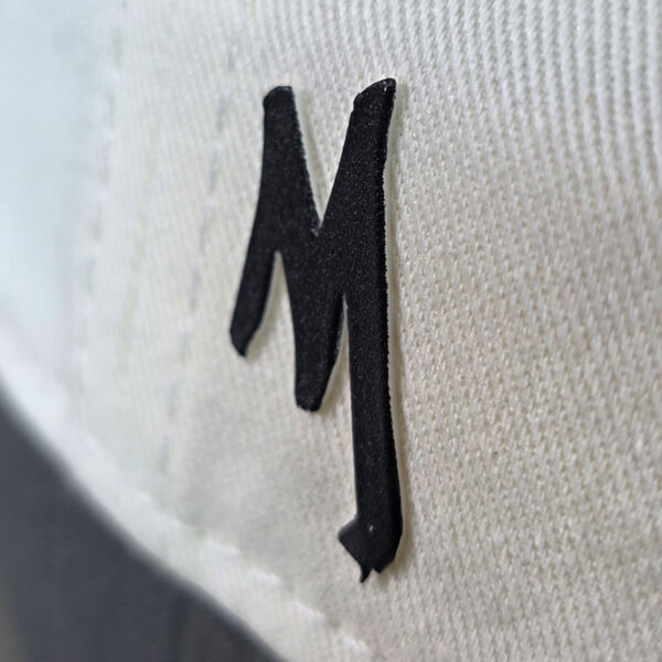 close up of an black MIB logo M on the side of a cream cap.