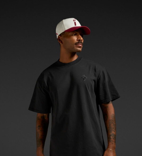 erson wearing a black MiB T‑shirt and a white and maroon MiB cap against a dark background.