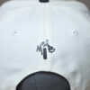 small embossed MIB drip print logo on the back of a cream cap